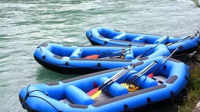 3 blue river rafting boats and paddles on the shore