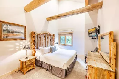 The primary suite has a log cabin feel wtih a king sized bed, an oversized dresser, a flat screen tv, and 2 nightstands