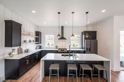 Gourmet kitchen featuring custom lighting, white quartz waterfall edge breakfast bar, high end appliances, everything is here