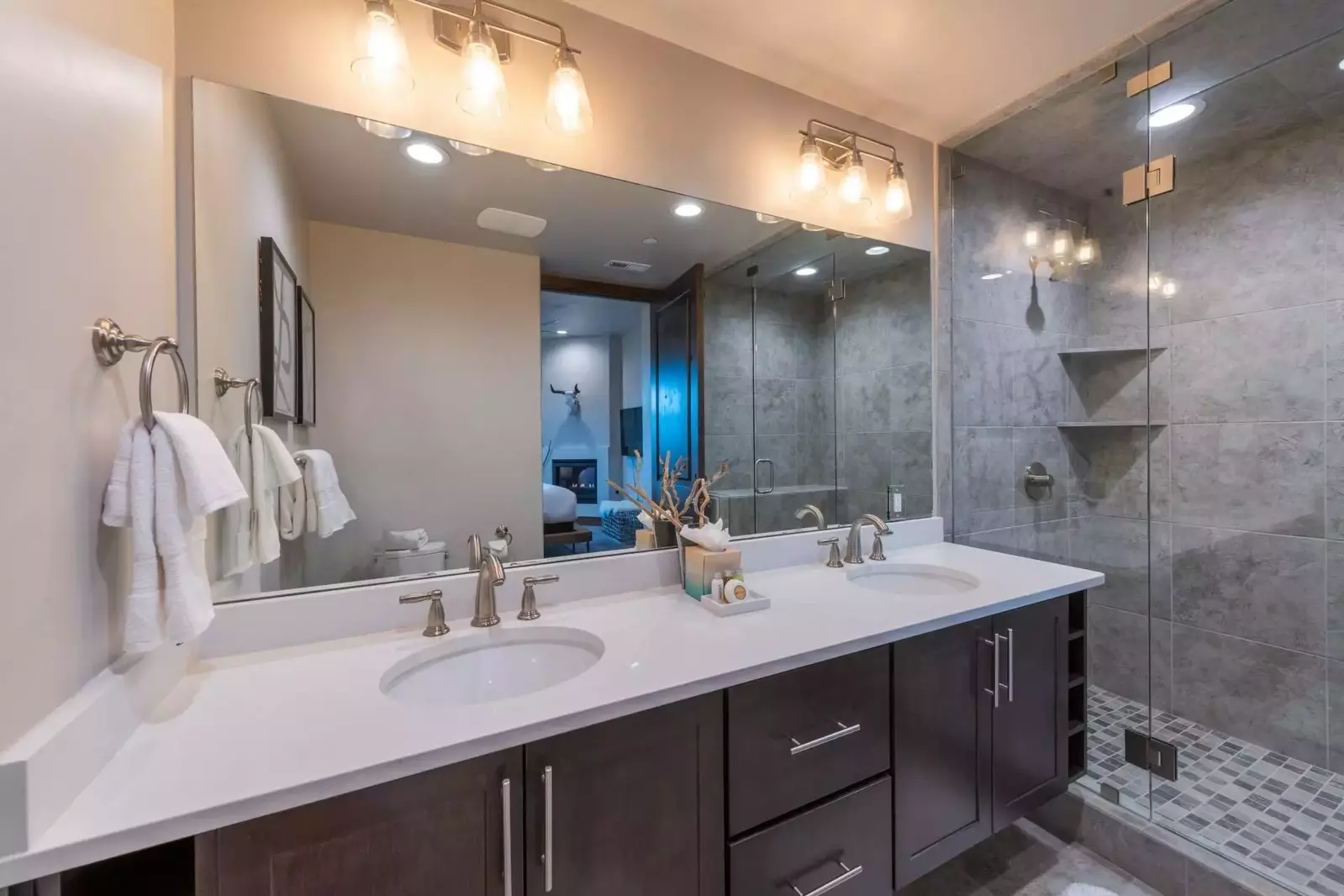 The primary suite bathroom feels like your own private spa, with large white quartz countertops, hardwood cabinetry, custom walk in glass shower with