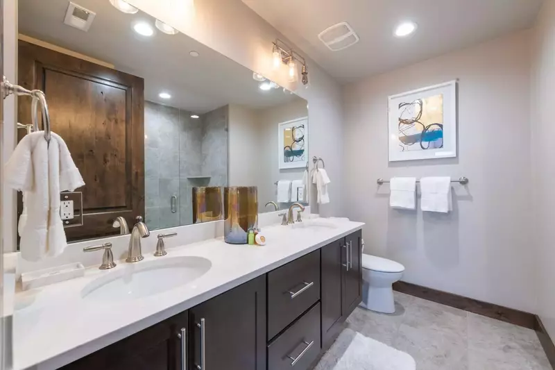 The guest bathroom is spacious with white quartz countertops, hardwood cabinetry and glass shower / tub combination.