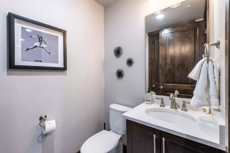 The luxurious powder room is perfect for guests with a white quartz sink and hardwood cupboards located just off the kitchen
