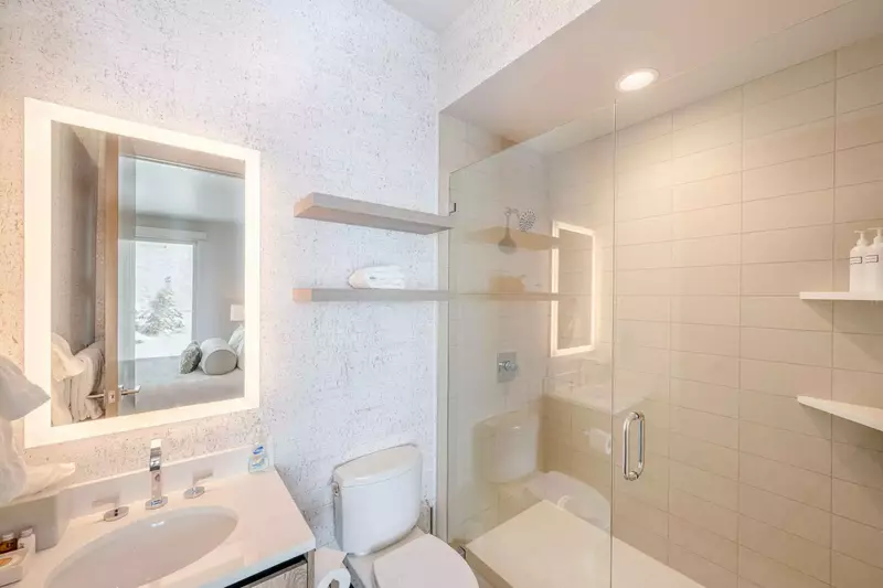 The first guest en-suite bathroom features an oversized walk in glass shower, toilet and marble topped vanity with an LED bac