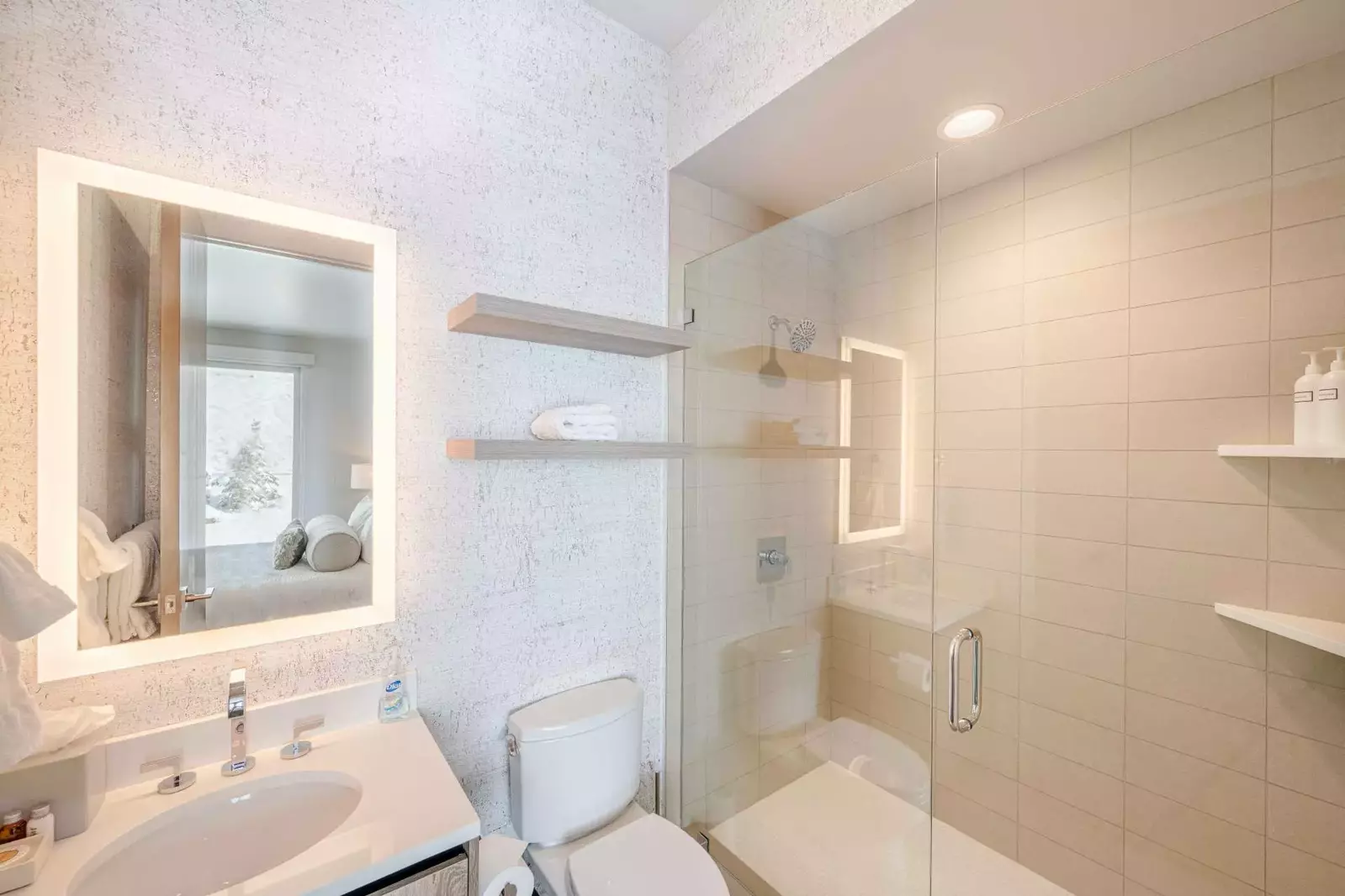 The first guest en-suite bathroom features an oversized walk in glass shower, toilet and marble topped vanity with an LED bac