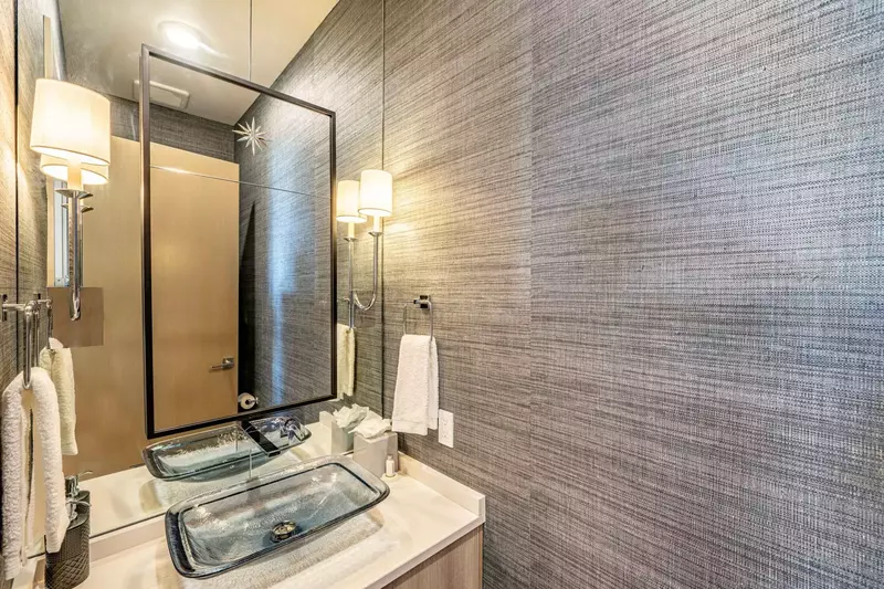 The elegant powder room is perfect for guests. Featuring high end appliances, custom glass sink with beveled glass mirror and dark grey linen wallpape