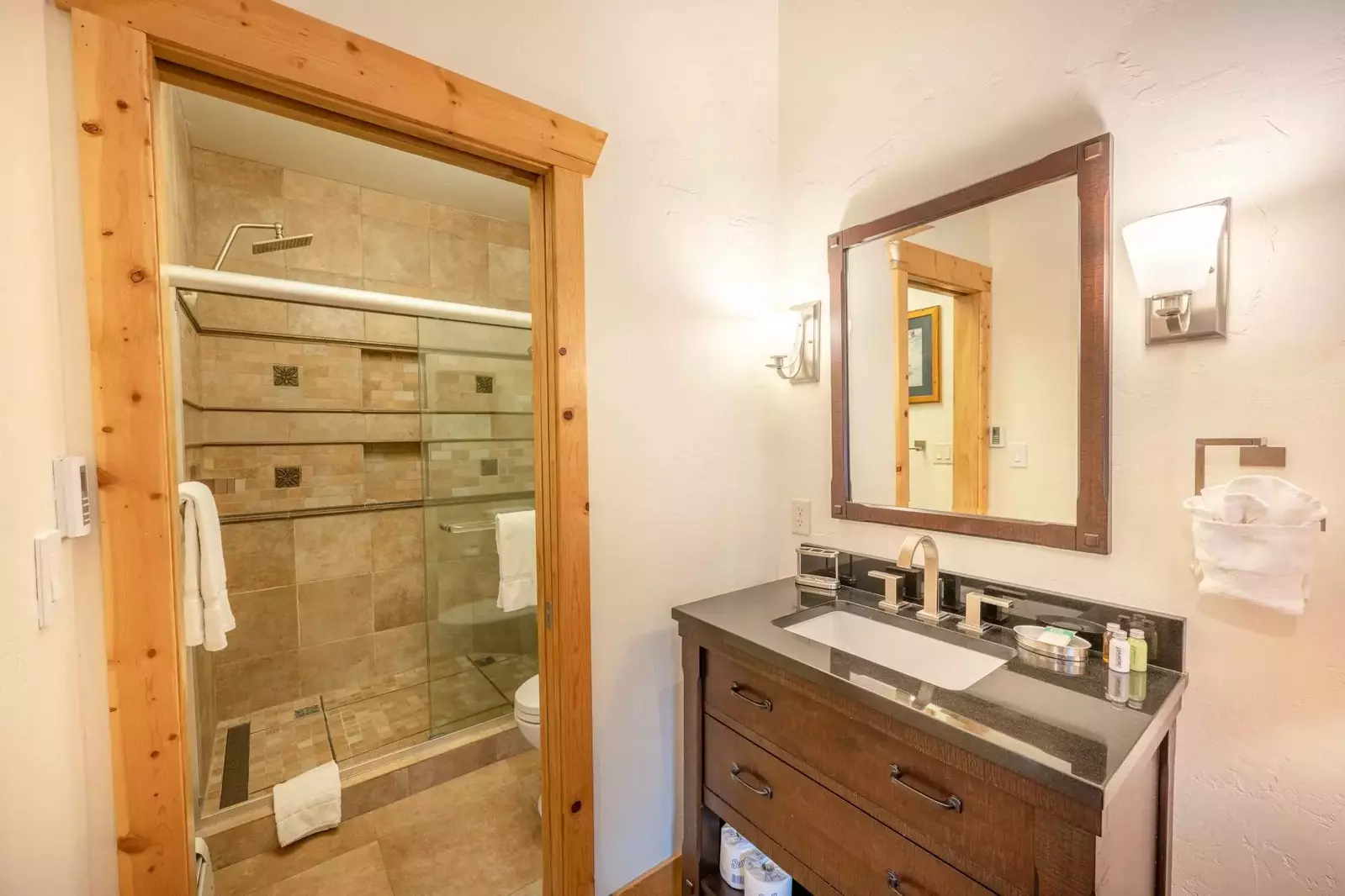 The primary en suite bathroom has a beautiful hardwood vanity that is topped with a granite counter top; There is a walk in glass shower with custom t