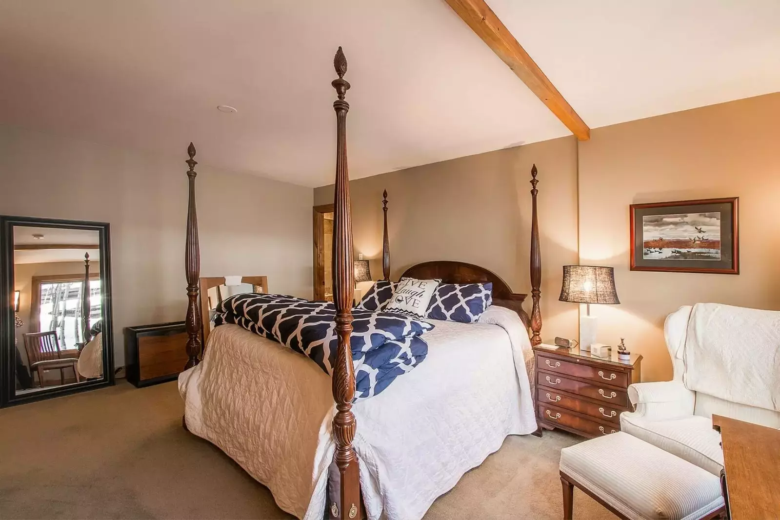 A large mirror reflects upon the lush bedding and furnishing in the master bedroom.