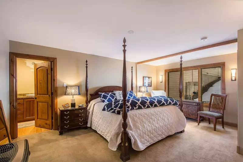 An elegant four-post king bed rests upon plush carpet with decorative chair and ensuite bathroom. Truly a royal master bedroom.