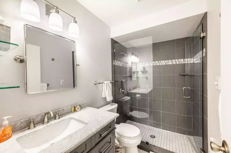 Located in the hallway - this newly updated full bathroom features an oversized hardwood vanity with a marble top, glass shelving and a tiled walk in