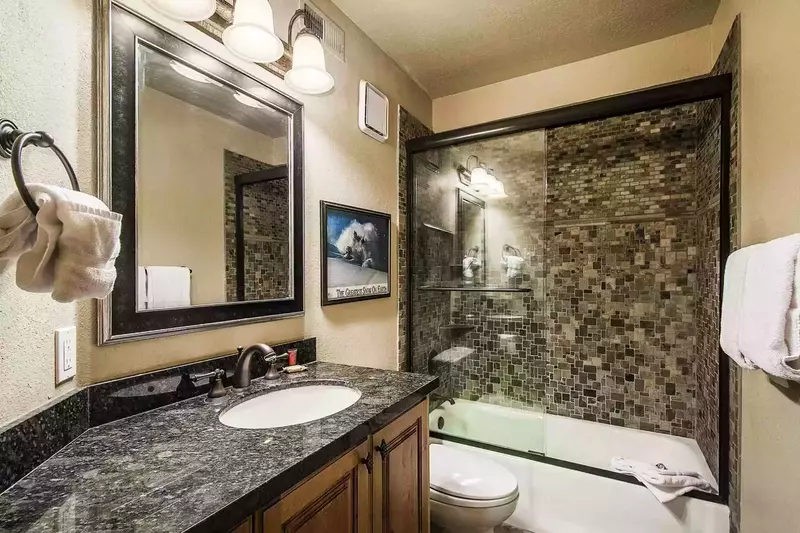 The en suite bathroom has a glass shower, granite countertop and bronze finishes.