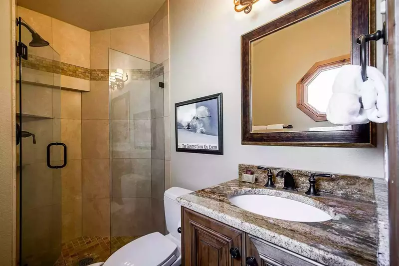 The en suite bathroom for BEDROOM #2 offers guests a walk-in glass shower with sandstone tiling, granite countertop with sink, and a toilet.