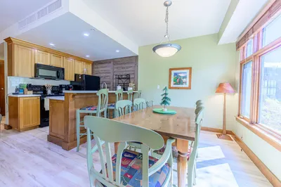 Open-concept kitchen and dining area with full-size table, breakfast bar, and large windows for natural light.