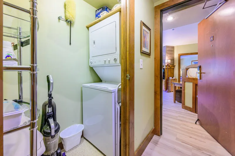 In-unit laundry closet with stacked washer and dryer, plus cleaning and storage essentials for extended stays.