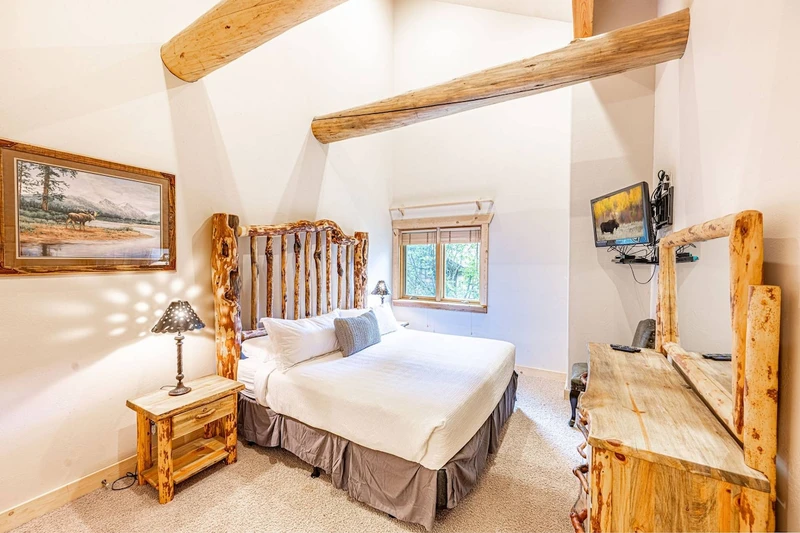 The primary suite has a log cabin feel wtih a king sized bed, an oversized dresser, a flat screen tv, and 2 nightstands