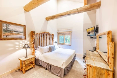 The primary suite has a log cabin feel wtih a king sized bed, an oversized dresser, a flat screen tv, and 2 nightstands