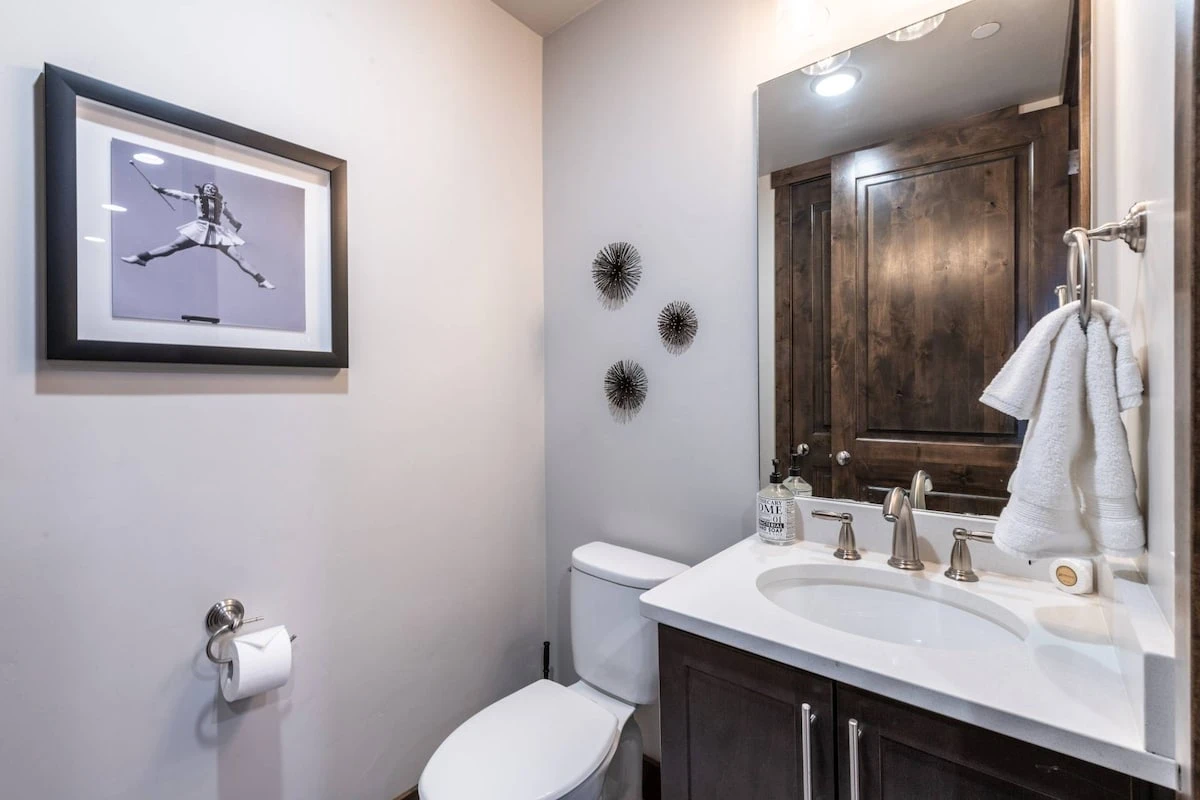 The luxurious powder room is perfect for guests with a white quartz sink and hardwood cupboards located just off the kitchen