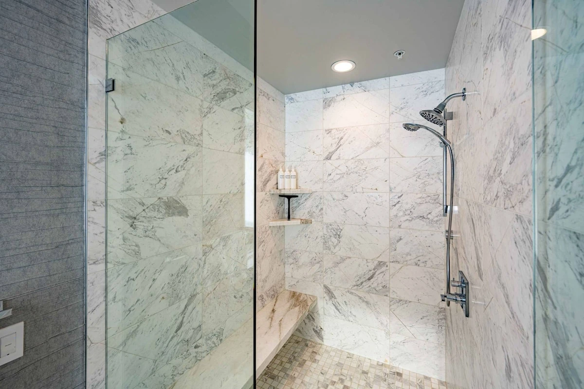 Guests can indulge in exquisite self care while staying at Apex - This Walk in Glass Shower with Carrara marble bench and tiles is located in the Prim