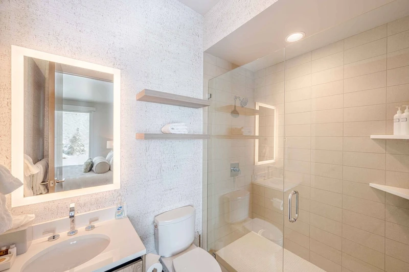 The first guest en-suite bathroom features an oversized walk in glass shower, toilet and marble topped vanity with an LED bac